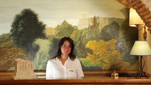 A reception desk with a mural of a landscape behind it, a lamp, and a small statue on the desk. - Hotel Residenza San Calisto (Rome)