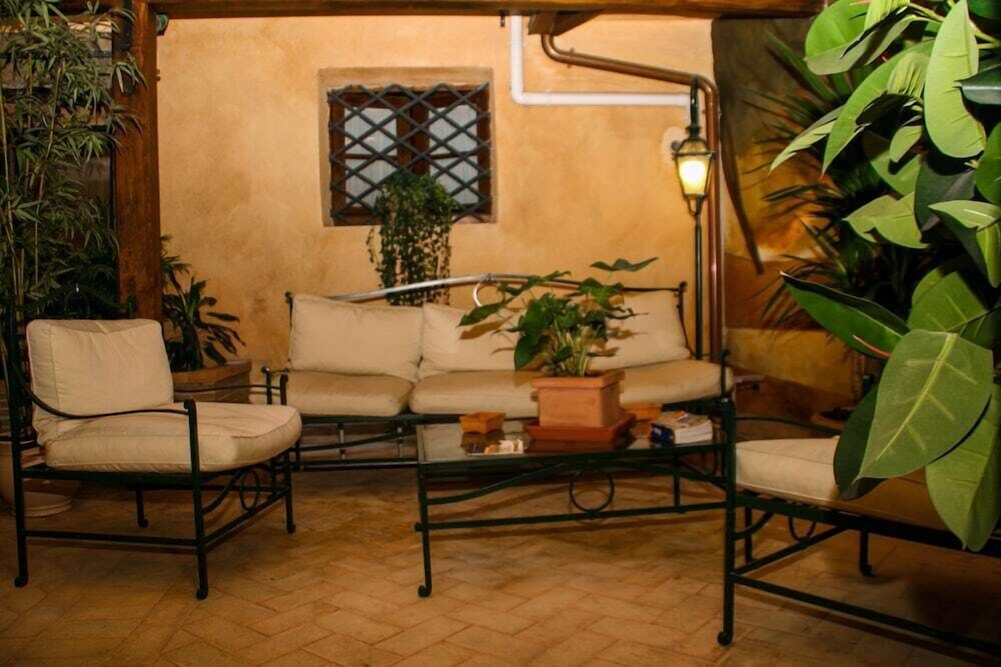 Un espace extérieur accueillant, aménagé avec un canapé et des fauteuils, entouré de plantes en pot et agrémenté d’une lampe.