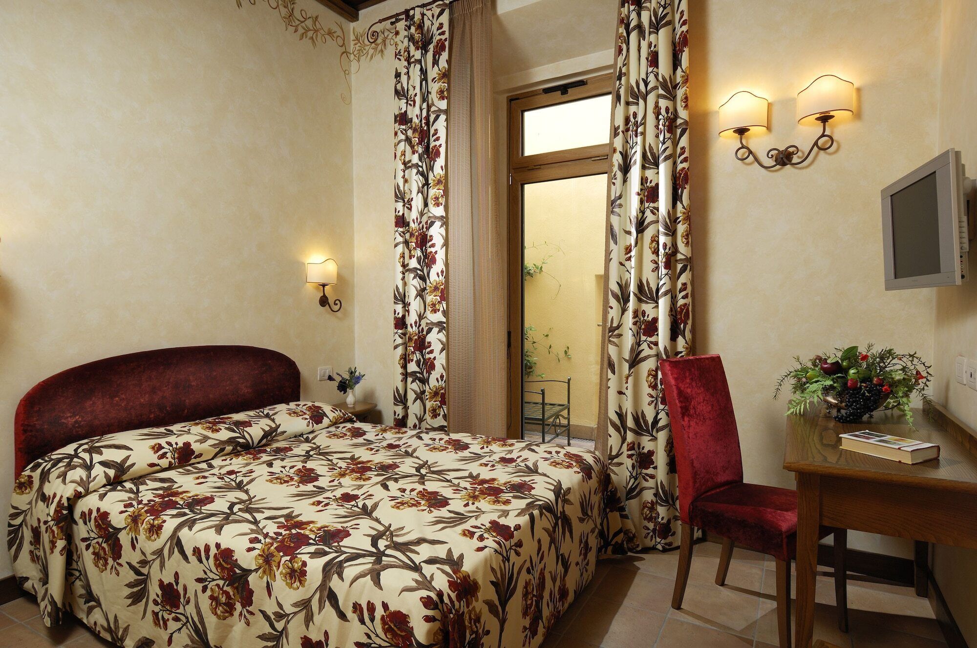 Habitació d'hotel amb un llit, un escriptori amb una cadira, una televisió i una finestra amb cortines.