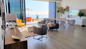 A modern living room with a sofa, armchairs, a dining table, and a kitchen area. - Villa Brava Atlântico (Ribeira Brava)