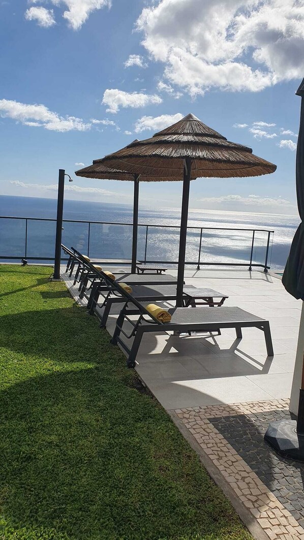 Una terraza con tumbonas y un paraguas de paja, con vistas a un cuerpo de agua.