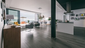 A modern living area with a wooden desk, a sofa, and a dining table. There is a large window with a view of the outdoors. - Villa Brava Atlântico (Ribeira Brava)