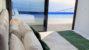 A bedroom with a large bed, white and green pillows, and a view of the ocean through a glass door. - Villa Brava Atlântico (Ribeira Brava)