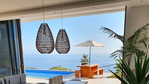 A modern dining area with a wooden table and chairs, a sofa, and a view of the ocean. - Villa Brava Atlântico (Ribeira Brava)