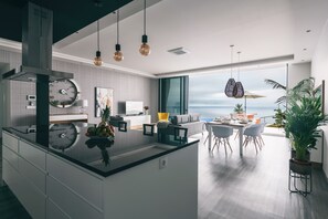 A modern kitchen with a central island, a dining area with a view, and a living space with a large window overlooking the ocean.