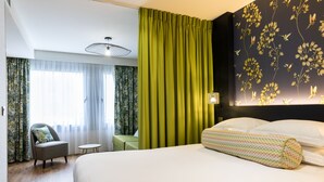 A hotel room with a large bed, a green curtain, a chair, a small table, and a wall with floral wallpaper. - Cadet Residence (Paris)