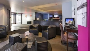 Un hall d’entrée moderne avec des espaces de détente, un comptoir d’accueil et un écran de télévision.