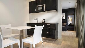 Une cuisine moderne avec des meubles noirs, un plan de travail blanc et un four à micro-ondes en acier inoxydable. On y trouve également un coin repas avec des chaises blanches et une table.