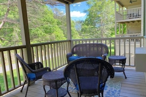 A covered outdoor area with wicker furniture, a view of trees, and a balcony with railings. - Apple Valley 3 at Rumbling Bald (Lake Lure)
