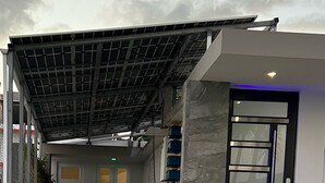 Una entrada de edificio moderna con un vestíbulo techado, una puerta con panel de vidrio y una pared de piedra.