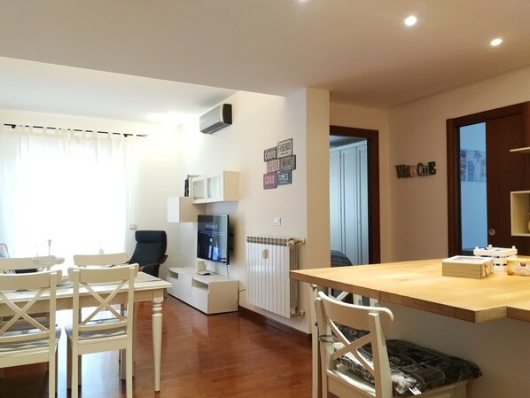 A modern living room with a dining area, a flat-screen TV, and a built-in air conditioning unit. - Marci's Home (Roma)
