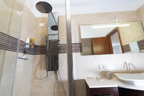 A modern bathroom with a glass-enclosed shower, a large mirror, and a white sink. - Marci's Home (Roma)