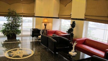 Eine Lobby mit einem roten Sofa, schwarzen Stühlen, einer Lampe und einer großen Topfpflanze.