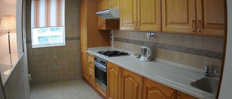 A kitchen with wooden cabinets, a stove, a sink, and a window with striped blinds.