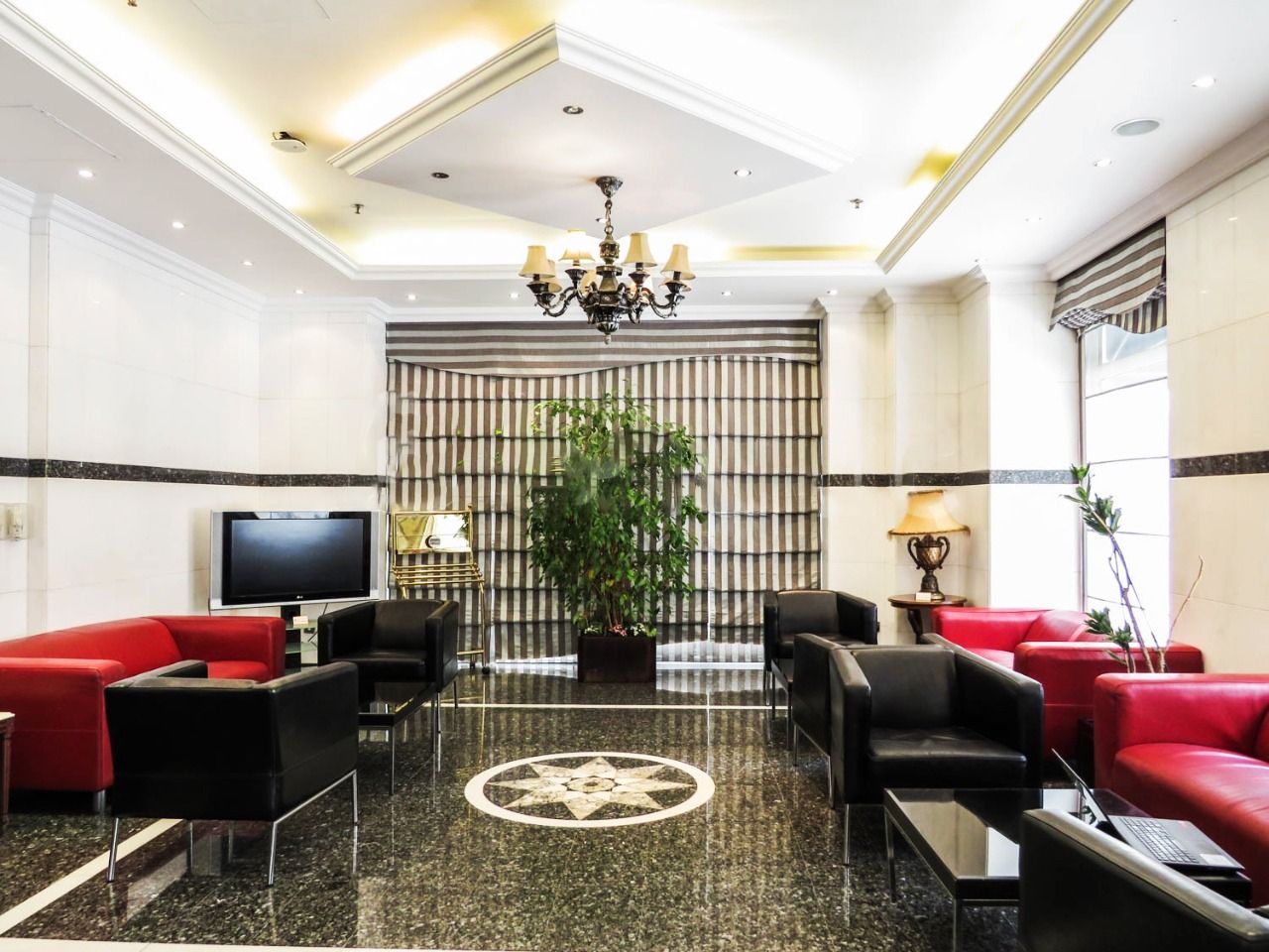 Eine Lobby mit Fernseher, roten und schwarzen Sofas, einem Chandelier und einer großen Pflanze.