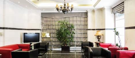 A lobby with a television, red and black sofas, a chandelier, and a large plant.