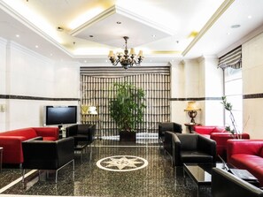A lobby with a television, red and black sofas, a chandelier, and a large plant.