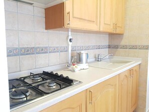 Una cucina con piano cottura a gas, una moka e pensili in legno.