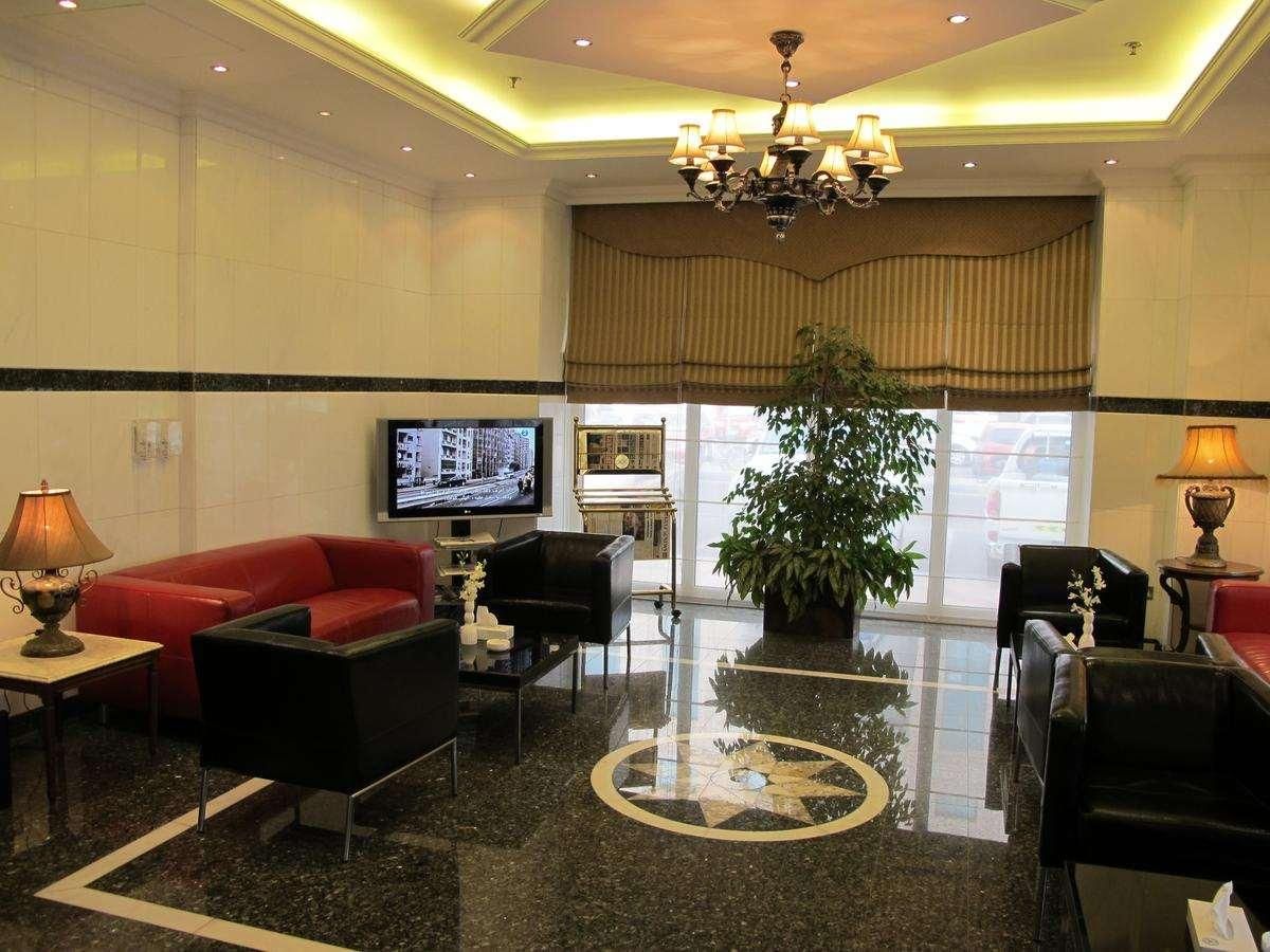 Eine Hotelhalle mit einem roten Sofa, schwarzen Sessel, einem Fernseher, einer großen Pflanze und einer Kristallleuchtreiter.