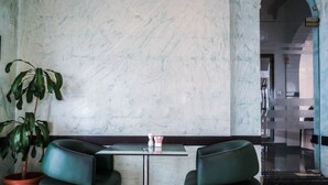 A lobby with a marble wall, a glass table, two green chairs, a potted plant, and a staircase in the background. - The Uptown Apartments Abu Dhabi by Gewan (Abu Dhabi)