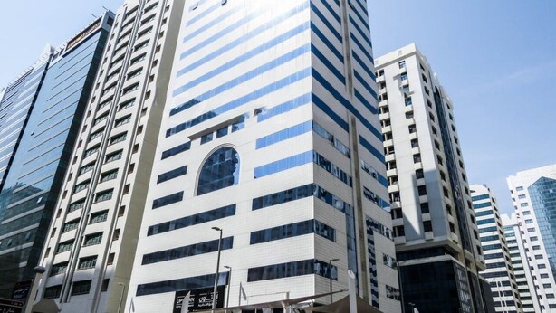 A high-rise building with a modern architectural design, featuring a prominent arched window and a series of balconies. - The Uptown Apartments Abu Dhabi by Gewan (Abu Dhabi)