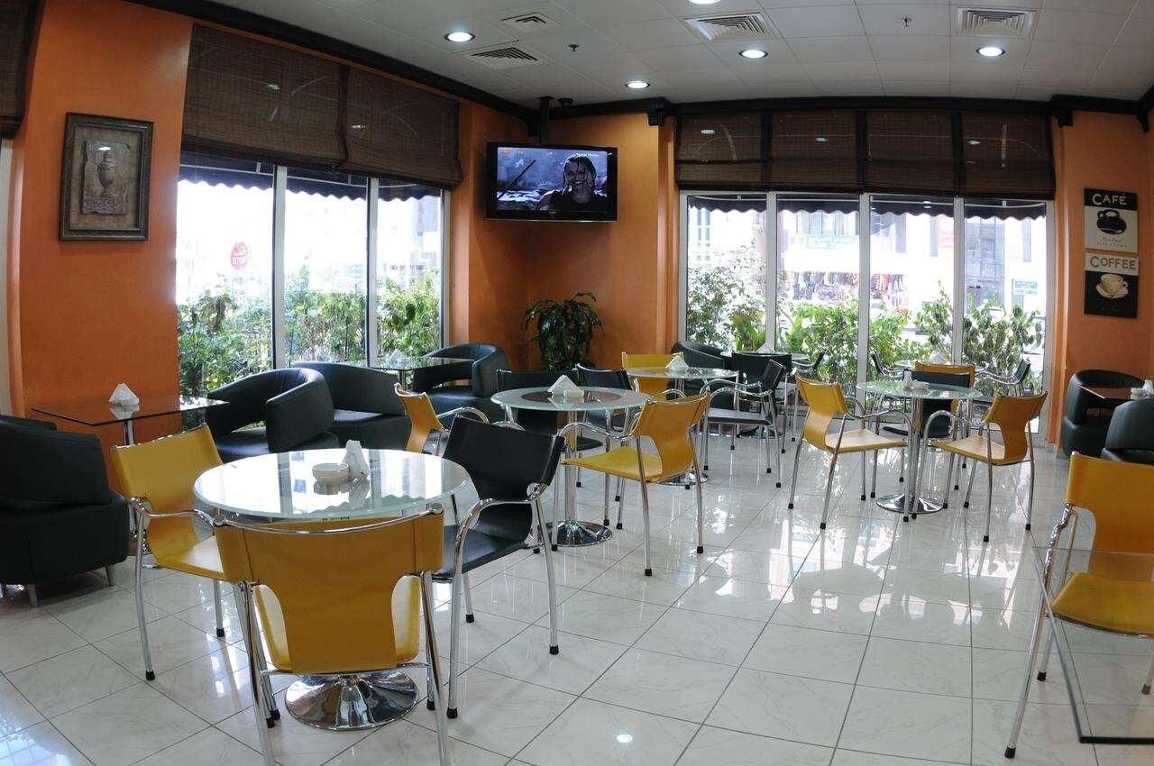 Ein Café mit runden Tischen und Stühlen, einem Fernseher an der Wand und großen Fenstern mit Jalousien.