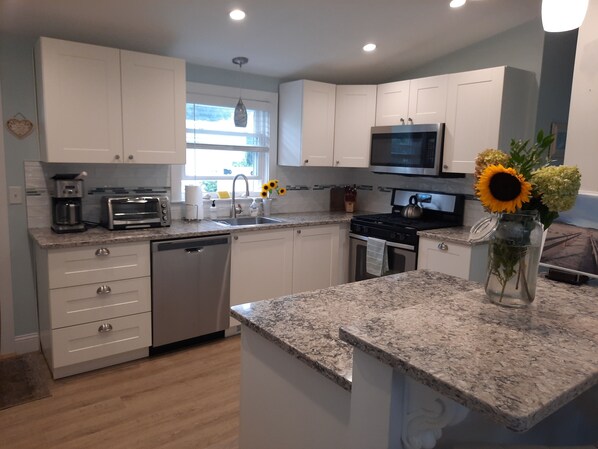 A modern kitchen with white cabinets, a granite countertop, a microwave, a stove, and a sink. - Seaside Escape just steps to Good Harbor beach in Gloucester (Gloucester)
