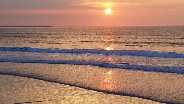 Een zonsondergang boven de oceaan, met golven die de kust naderen.