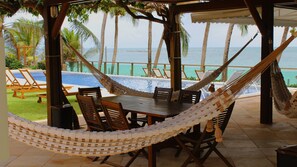 A hammock set up over a wooden table and chairs, with a view of a pool and palm trees. - Mansão felicidade pé na areia Jacumã RN (Ceara-Mirim)
