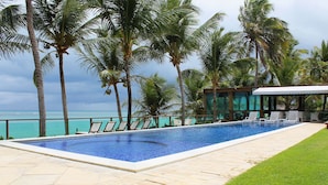 A swimming pool with lounge chairs, surrounded by palm trees and a view of the ocean.