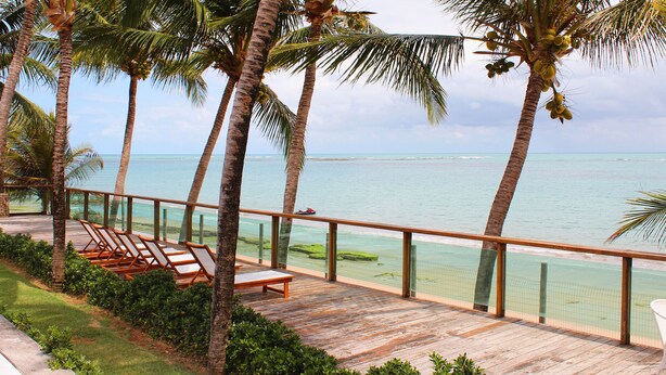 A wooden deck with lounge chairs overlooking a beach and ocean.