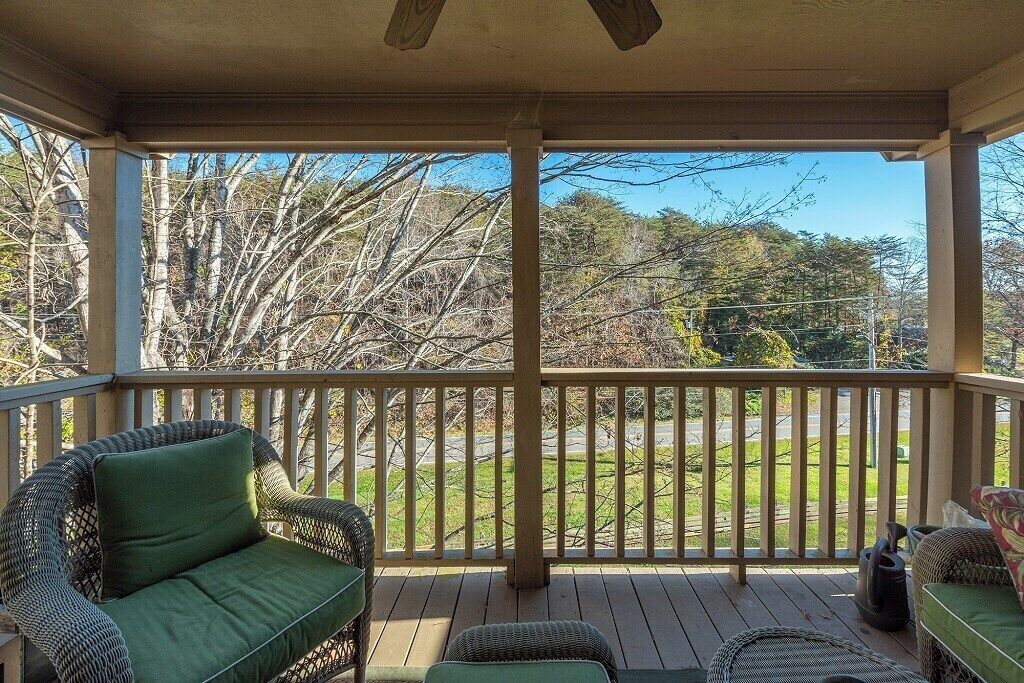 A covered porch with wicker furniture, a railing, and a view of trees and a road.