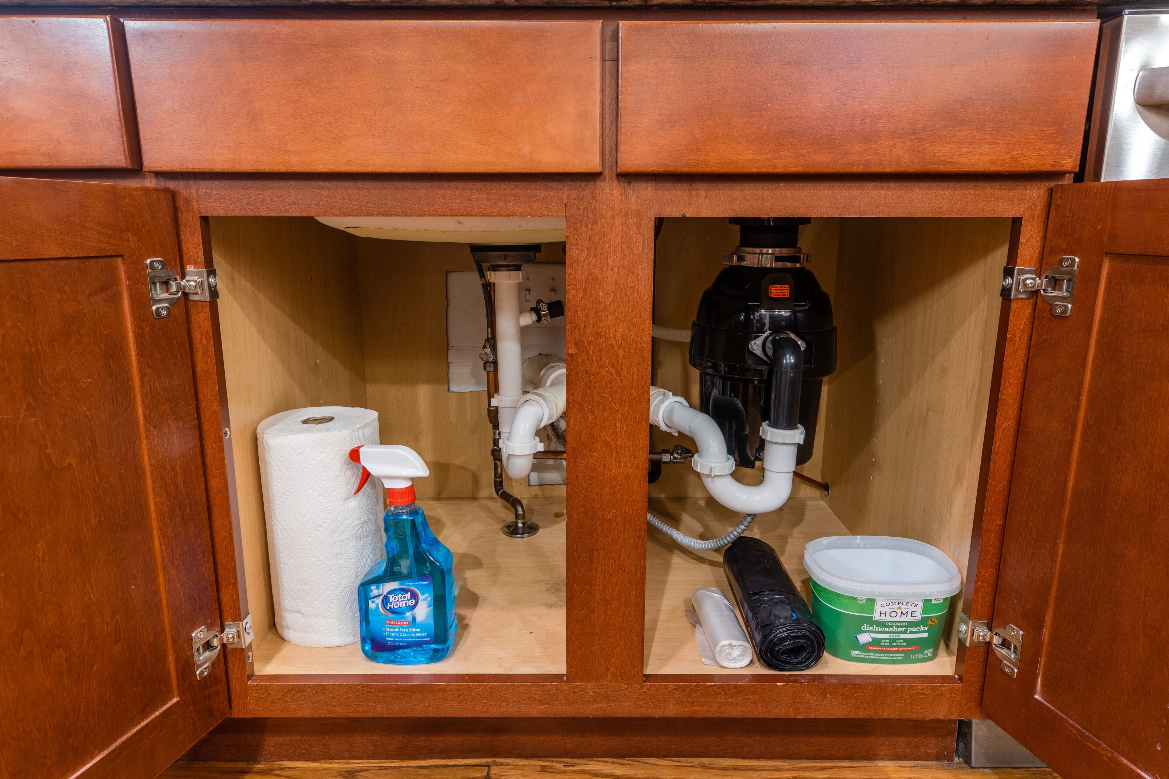 A wooden cabinet with a toilet paper roll, a bottle of dish soap, and a container of dishwashing liquid.