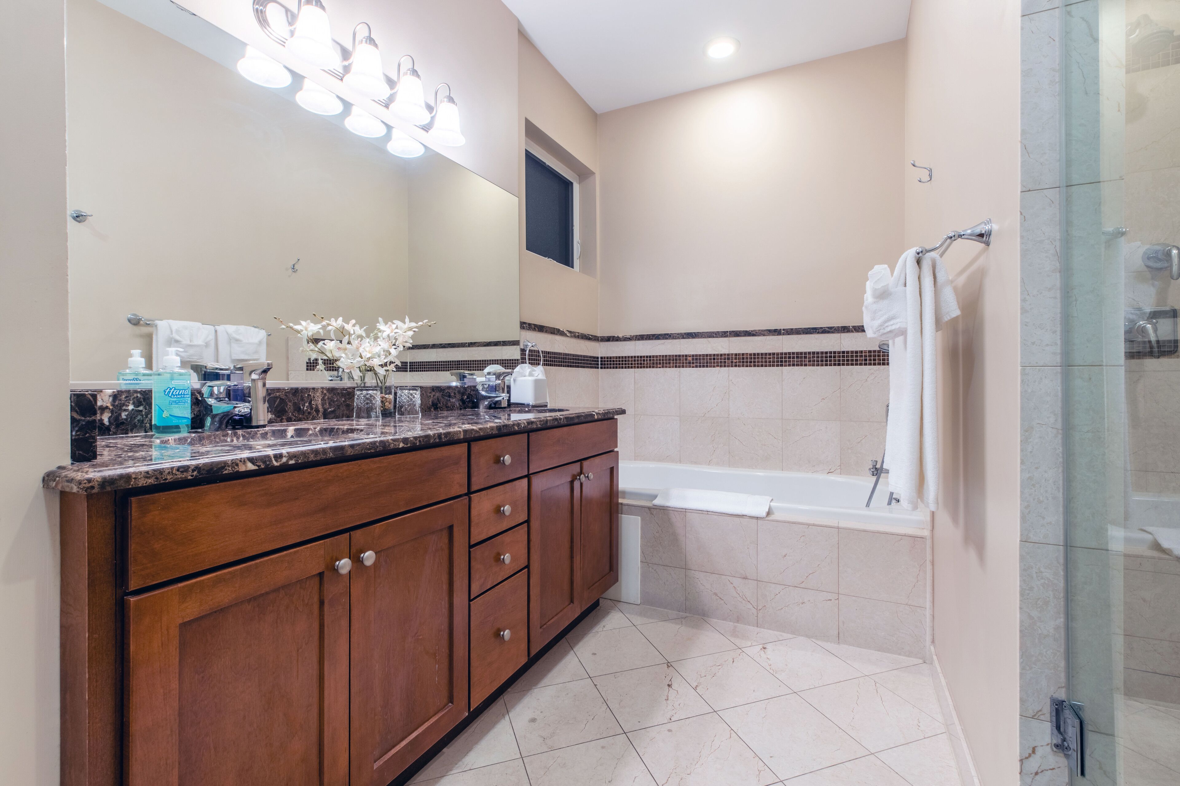 A bathroom with a marble countertop, a large mirror, a bathtub, and a shower area.