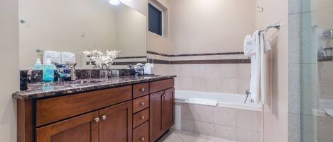 A bathroom with a marble countertop, a large mirror, a bathtub, and a shower area.