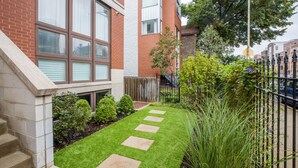 A residential building with a brick facade, large windows, and a small garden with stepping stones.