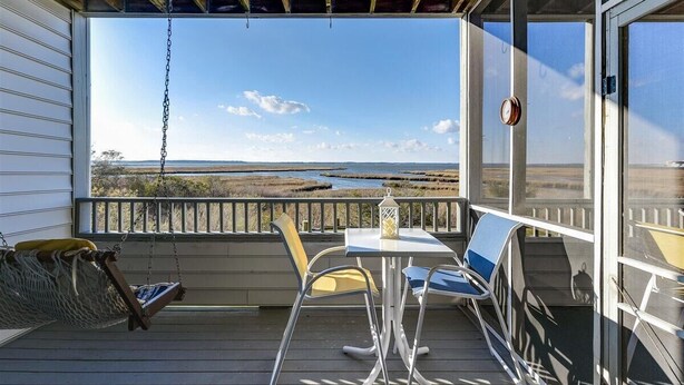 Ein Balkon mit Tisch und Stühlen, einer Hängematte und Blick auf eine Küstenlandschaft.