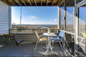 Varanda com mesa e cadeiras, uma rede pendurada e vista para a paisagem costeira.