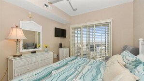 Ein Schlafzimmer mit Bett, Kommode, Fernseher und Fenster mit Jalousien.