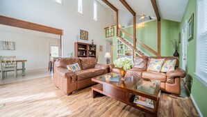 A spacious living room with a wooden floor, two leather sofas, a coffee table, and a staircase leading to an upper level.