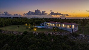 Ein großes, modernes Haus mit rotem Dach, umgeben von üppiger Vegetation und einem Pool.