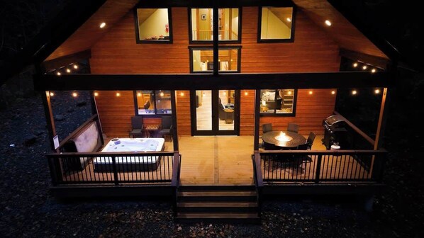 A wooden cabin with a deck, a hot tub, and a barbecue area.