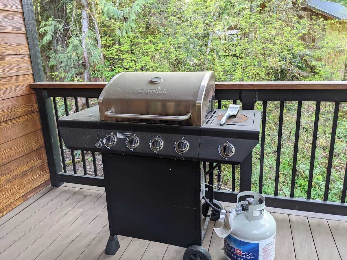 A barbecue grill on a wooden deck with a gas tank nearby.