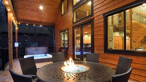 Una terraza de madera con una mesa redonda y sillas, un jacuzzi y una escalera que lleva a un nivel superior.