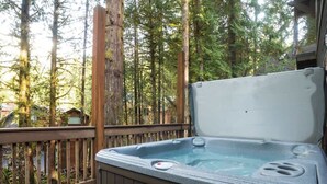 Un jacuzzi en una terraza de madera con vistas a un bosque.