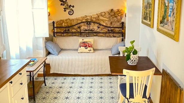 Un dormitorio acogedor con cama, escritorio y silla. Se observa una pared de piedra detrás de la cama y un candelabro sobre ella.
