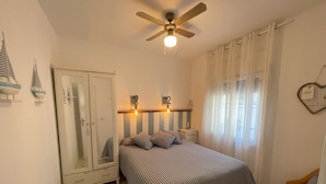 Un dormitorio con cama, armario, ventilador de techo y mesita de noche.