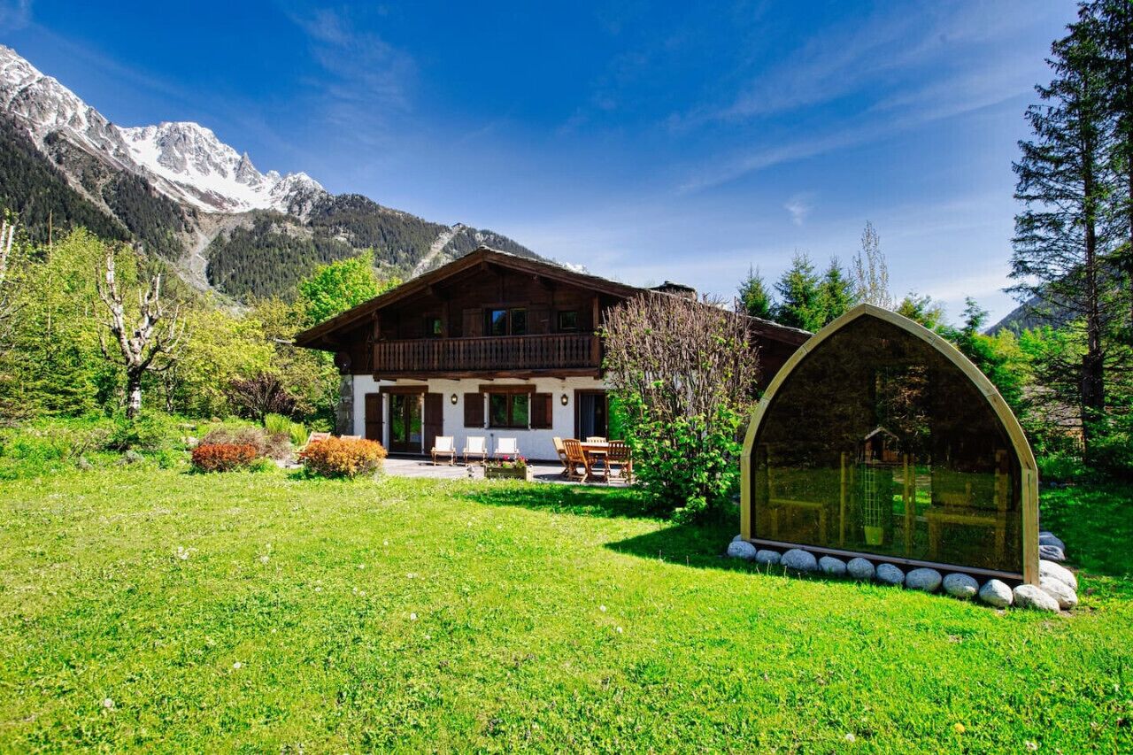 Een houten chalet met een balkon, omgeven door een weelderig groen gazon en een berg op de achtergrond.