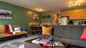 A cozy living room with a sofa, coffee table, and a dining area with chairs. - Apex Mountain ~ Beaconsfield Getaway (Apex Mountain Resort)
