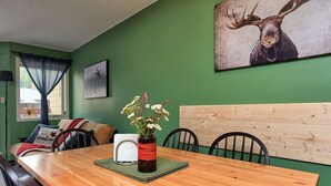 A dining area with a wooden table, chairs, a vase with flowers, and a painting of a moose on the wall. - Apex Mountain ~ Beaconsfield Getaway (Apex Mountain Resort)